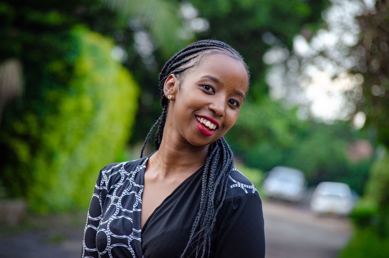 A joyful woman with braided hair smiling outdoors in a summer setting.