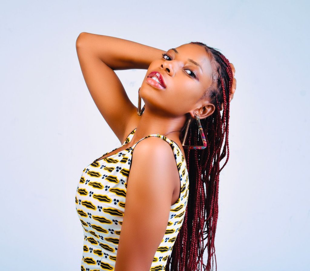 Elegant young woman posing in studio with vibrant braided hair and geometric earrings.