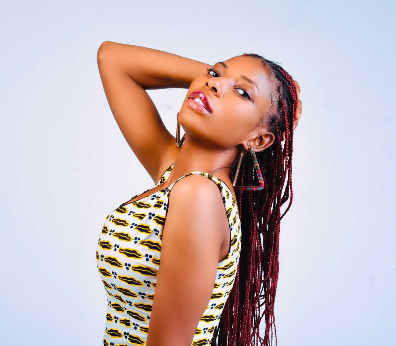 Elegant young woman posing in studio with vibrant braided hair and geometric earrings.