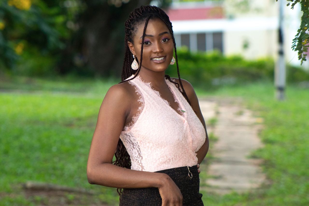 Outdoor portrait of a smiling young woman in a pink lace top in Kumasi, Ghana.