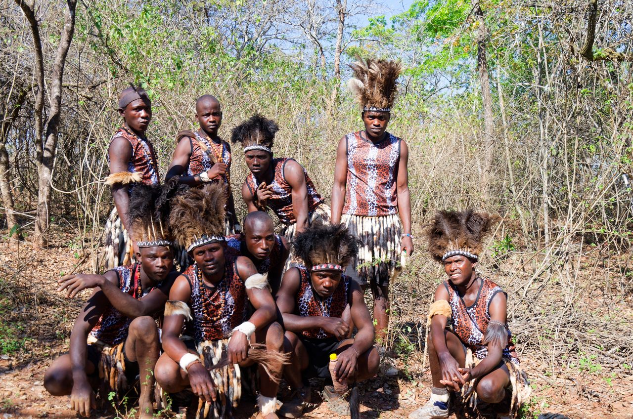 A group of men in traditional Zimbabwean attire posed in a forest clearing.