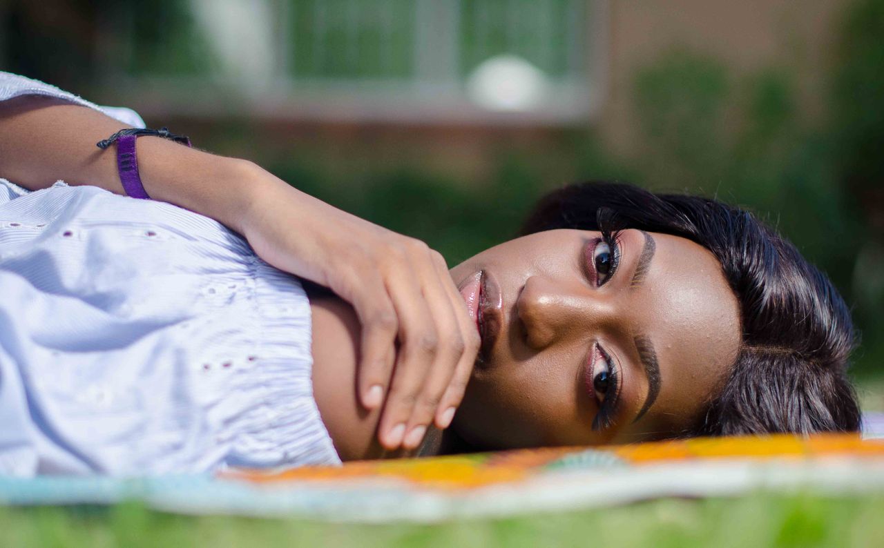Beautiful woman lying on grass, gazing sideways with a serene expression outdoors in summer.